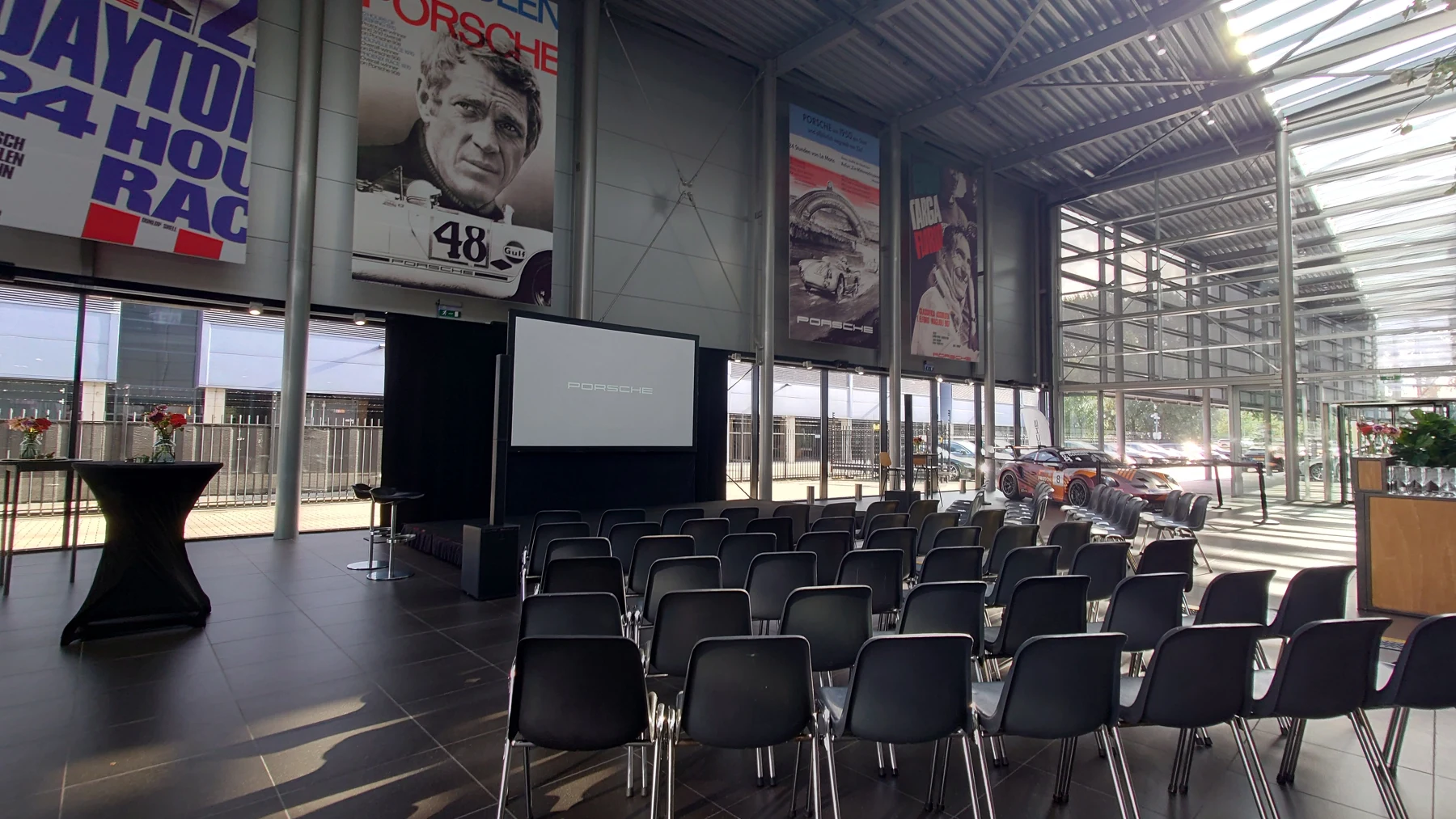 Symposiumopstelling met stoelen, podium en projectiescherm bij Porsche Amsterdam