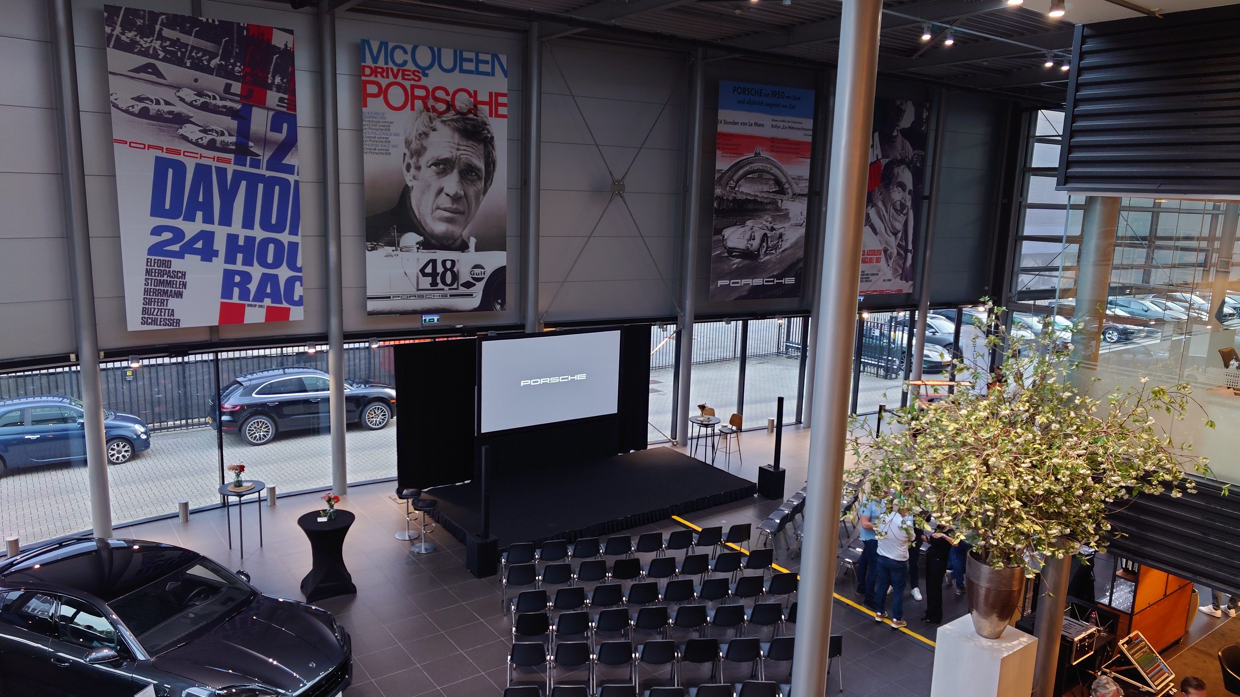 Symposiumopstelling met podium en projectiescherm in een Porsche-showroom